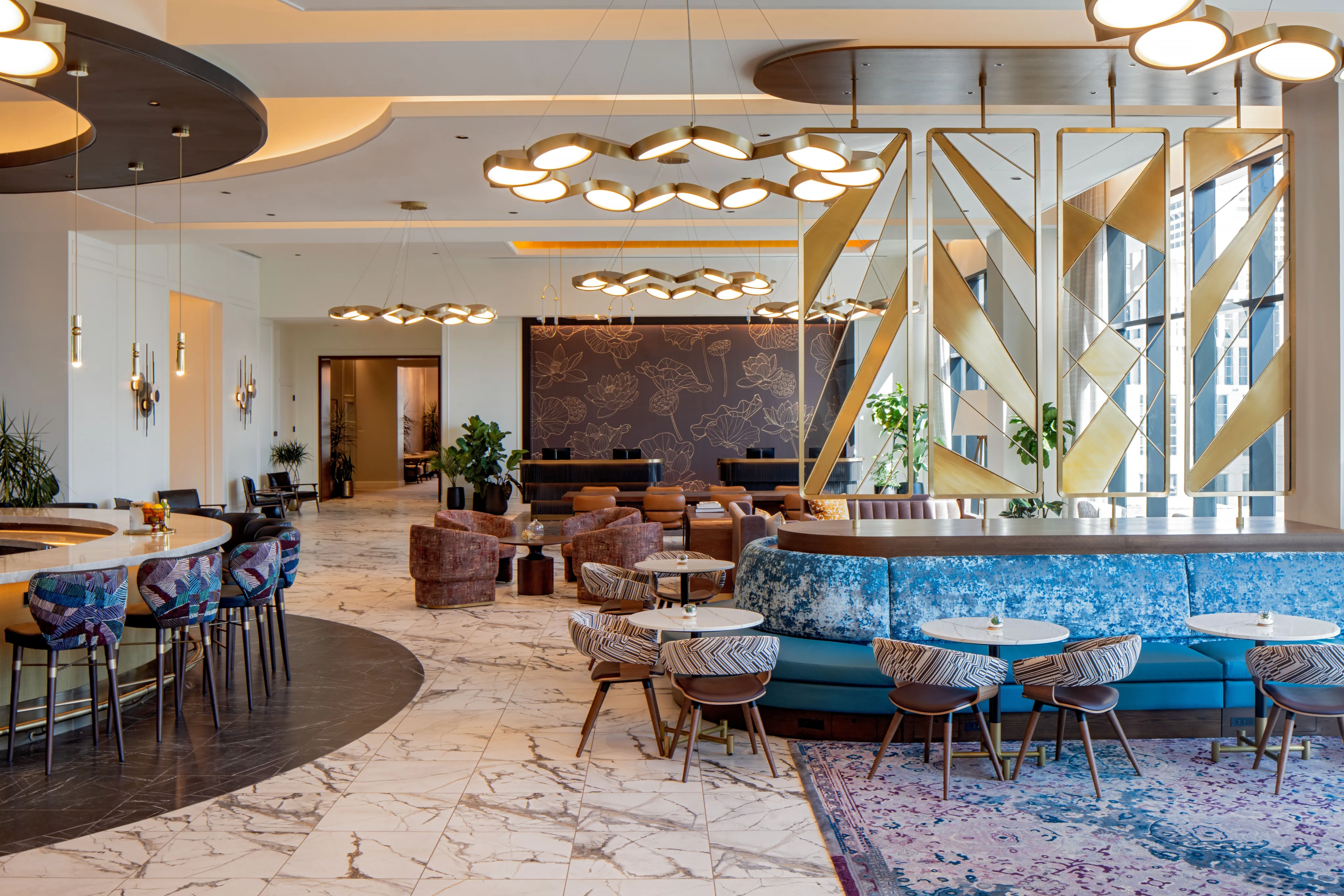 The Lovelorn Lounge features marble floors, stylish seating areas, decorative light fixtures, gold geometric room dividers, and large windows that flood the modern space with natural light.