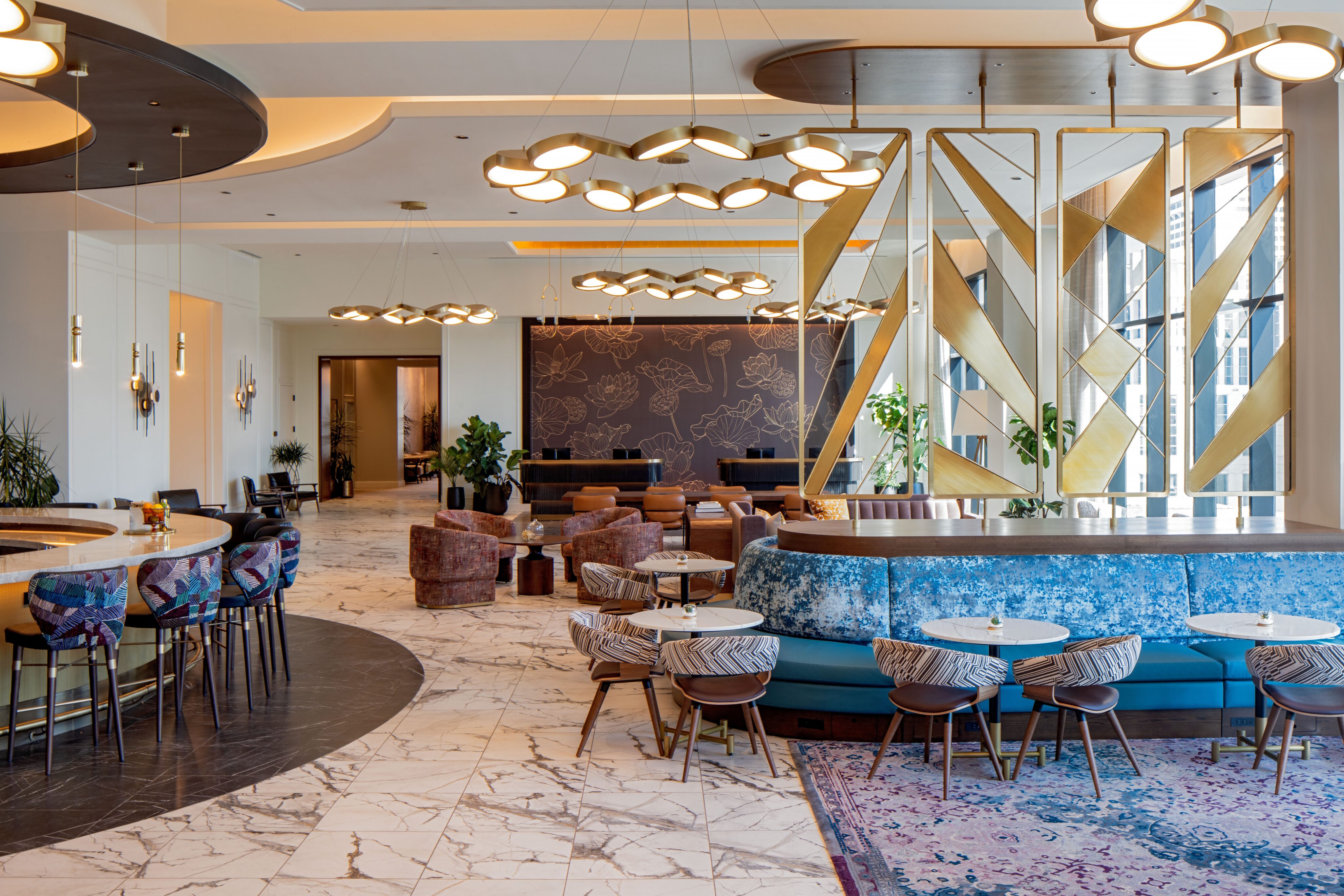 The Lovelorn Lounge features marble floors, stylish seating areas, decorative light fixtures, gold geometric room dividers, and large windows that flood the modern space with natural light.