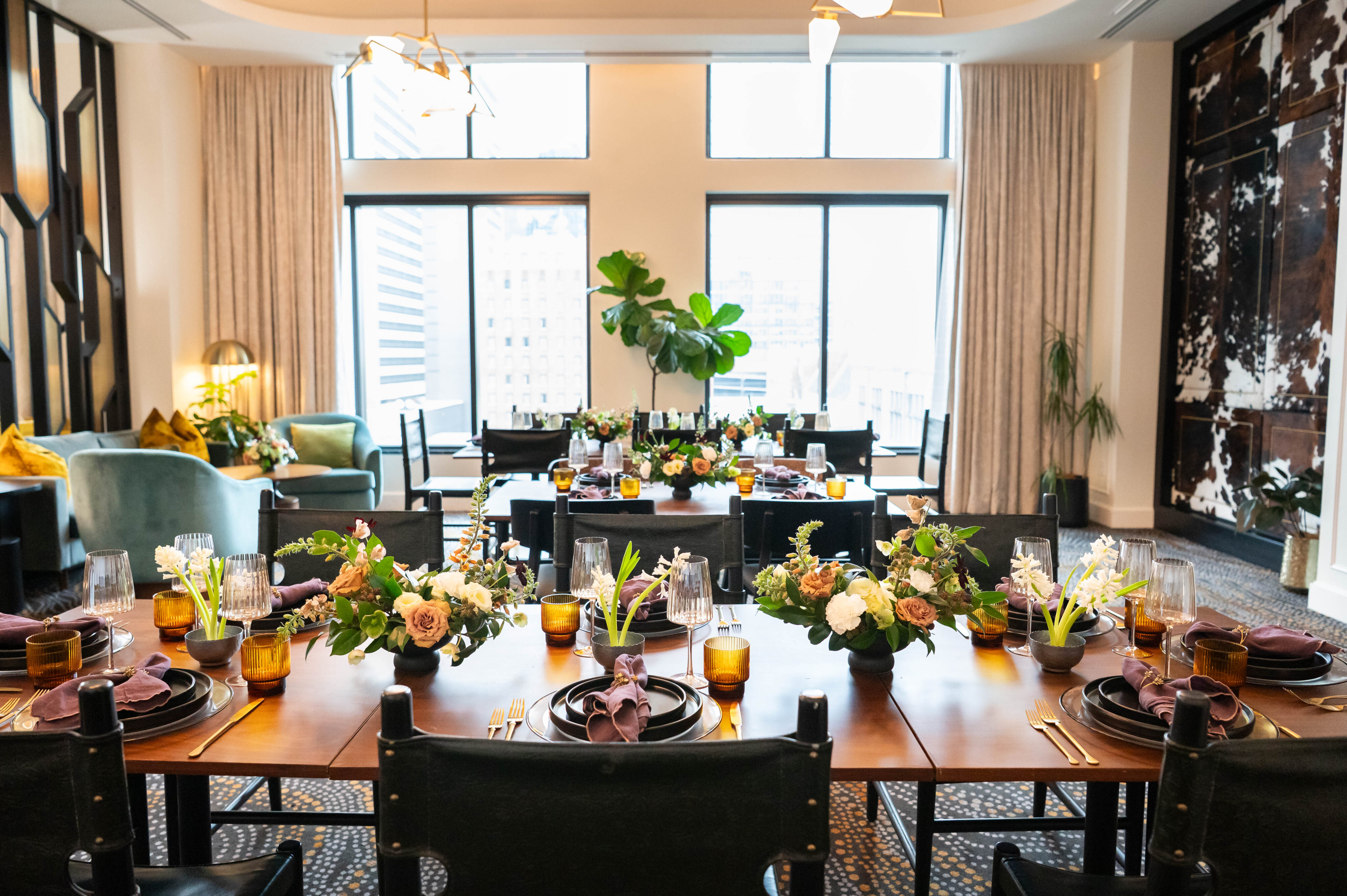 Elegant dining room at the Lovelorn Lounge with decorated tables set for a formal meal, featuring floral centerpieces, sparkling glassware, and large windows in the background.